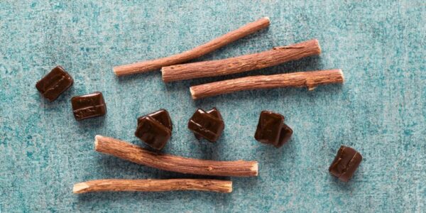 Raízes secas de Glycyrrhiza glabra ao lado de balas de alcaçuz, mostrando a matéria-prima usada tanto em preparações medicinais quanto na indústria de doces