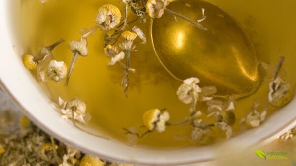 Uma xícara com chá de camomila quente, decorada com flores frescas ao lado. A cor dourada do chá e o vapor subindo criam uma atmosfera acolhedora e relaxante.