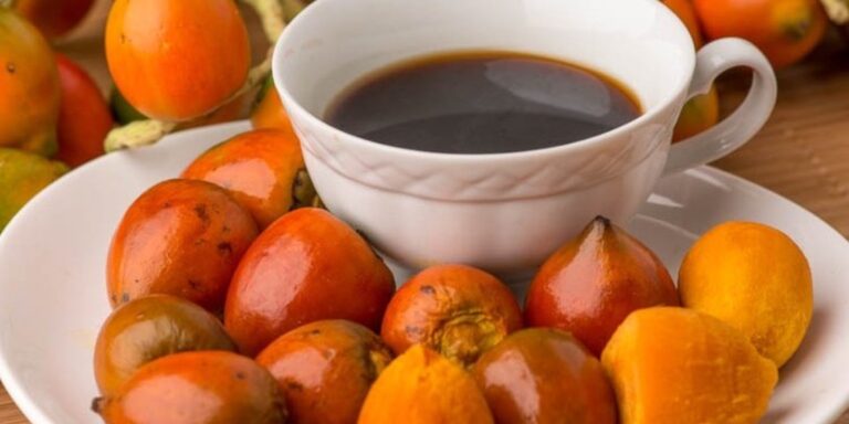 Frutos de pupunha crus, de casca vermelha e alaranjada, ao lado de uma xícara de café